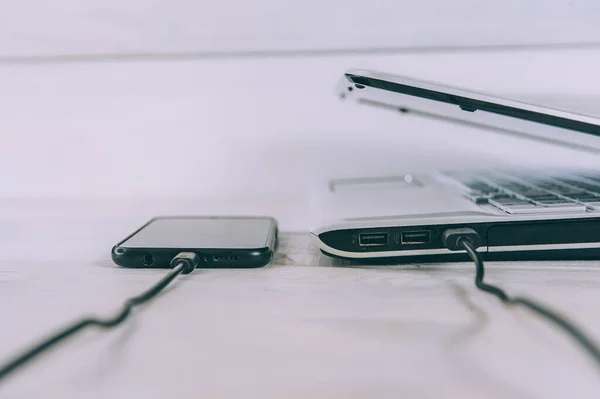 Akıllı Telefon Beyaz Ahşap Bir Masada Dizüstü Bilgisayardan Şarj Oluyor — Stok fotoğraf