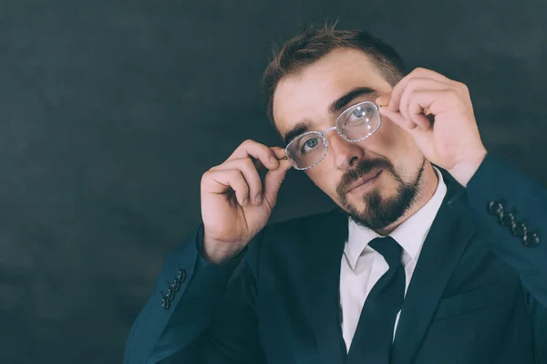 Gömlekli ve kravatlı bir iş adamı, elinde gözlüklerle karanlık bir arka planda.