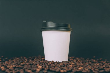 Arka planda kahve çekirdekli tek kullanımlık kahve bardağı.