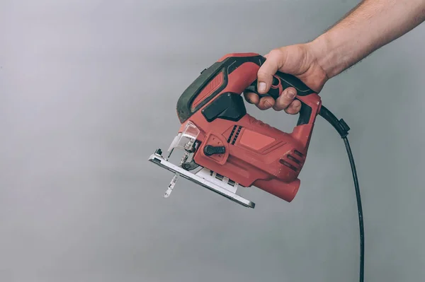 The guy holds a jigsaw in his hand, a power tool for working on metal and wood