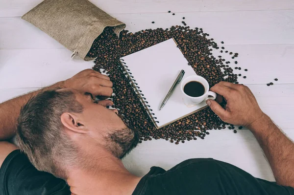 The guy fell asleep on the table, against the background of a cup with a notebook and coffee beans
