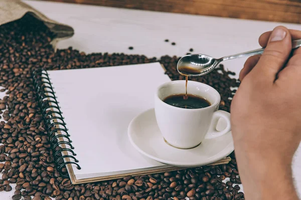 A man stirs coffee on a background of a notebook and beans