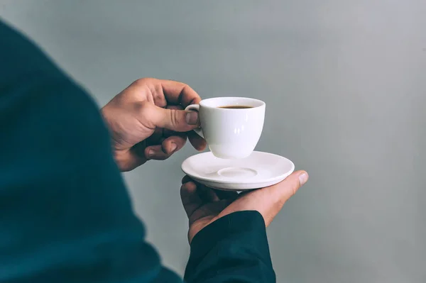 Ceketli iş adamı içer ve elinde gri arka planda kahve olan bir fincan tutar.