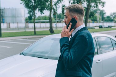 Mavi ceketli bir işadamı arabanın arka planında telefonla konuşuyor.