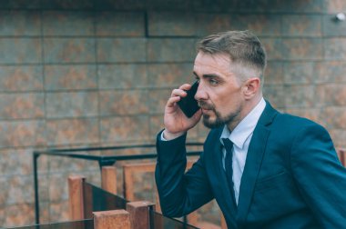 Mavi ceketli bir iş adamı ve arka planında bir akıllı telefon var.