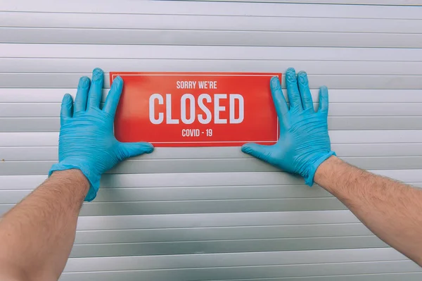 Sorry We\'re Closed COVID-19 A man in blue rubber medical gloves sticks a red plate