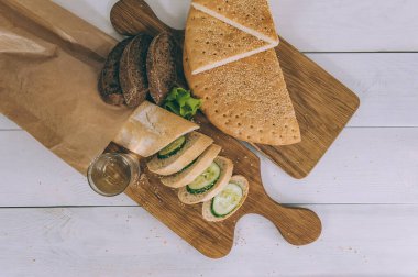 Masadaki mutfak tahtalarında salatalık ve marullu çeşitli ekmek çeşitleri var.