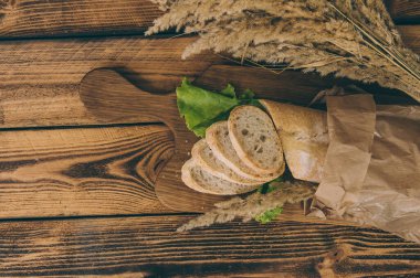 Kağıt ambalajda marullu taze ekmek, yanmış ahşap bir masanın üzerinde.