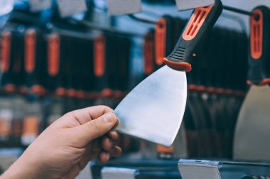 Hırdavatçıdaki alıcı malları seçer. Adamın biri elinde metal bir spatula tutuyor.