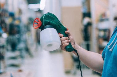 Adamın biri elinde elektrikli sprey tabanca tutuyor. Bir hırdavatçıda alıcı bir ürün seçer