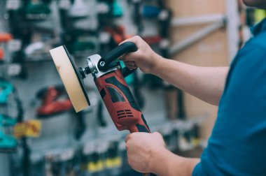 Bir adam elinde bir cilalama makinesi tutuyor. Bir hırdavatçıda alıcı bir ürün seçer