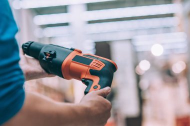 Delmek için elinde elektrikli matkap tutan bir adam. Bir hırdavatçıda alıcı bir ürün seçer