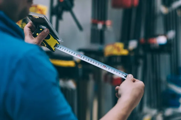 Hırdavatçıdaki alıcı malları seçer. Bir adam elinde metal bir mezura tutuyor.