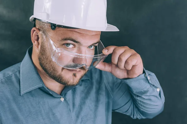 Güvenlik gözlüklü bir adam ve karanlık arka planda bir miğfer.