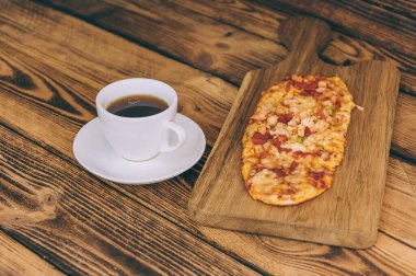 Tahta bir masada bir fincan kahveyle küçük bir pizza. Fast food evde pişiyor.