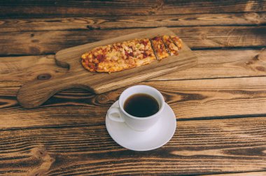 Tahta bir masada bir fincan kahveyle küçük bir pizza. Fast food evde pişiyor.