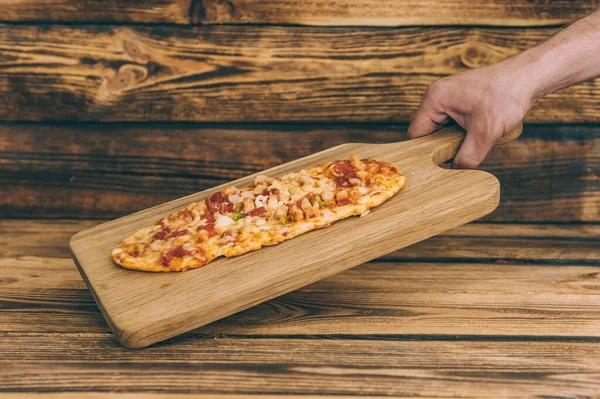 The guy holds pizza on a wooden table. Fast food cooked at home