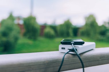 Taşınabilir şarj aleti, bir akıllı telefonu doğanın arka planına karşı şarj ediyor.