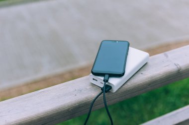 Taşınabilir şarj aleti, bir akıllı telefonu doğanın arka planına karşı şarj ediyor.