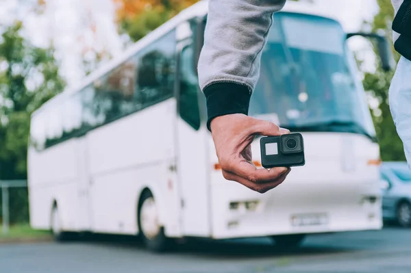 Blogger with an action camera in his hands, against the background of a bus