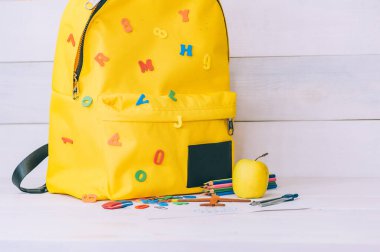 Okul konseptine geri dönelim. Ahşap arka planda ofis malzemeleri olan sarı bir sırt çantası.