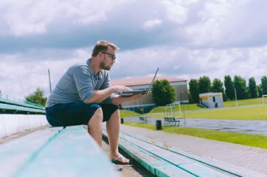 Adam dışarıda bir bankta dizüstü bilgisayarda çalışıyor.