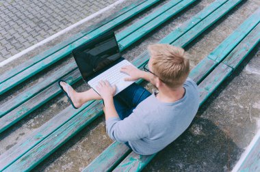 Adam dışarıda bir bankta dizüstü bilgisayarda çalışıyor.