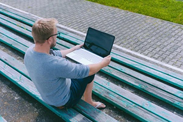 The guy works at a laptop on a bench outdoors against a background of grass