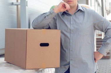 Elinde karton bir kutuyla gri takım elbiseli bir adam süpermarketin arka planında. Posta teslimatı konsepti