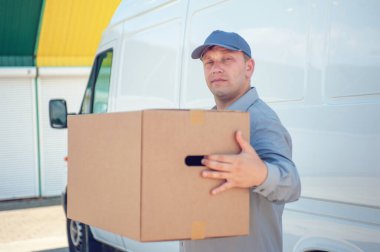 Elinde karton bir kutuyla gri takım elbiseli bir adam minibüsün arka planında. Posta teslimatı konsepti