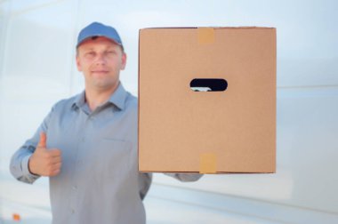 Elinde karton bir kutuyla gri takım elbiseli bir adam minibüsün arka planında. Posta teslimatı konsepti