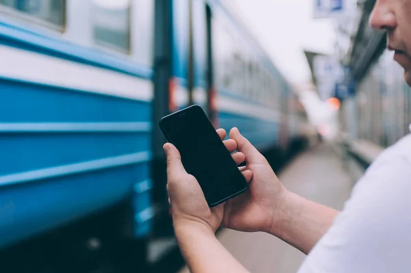 Adamın elinde tren istasyonundaki trenin arka planında akıllı bir telefon var.
