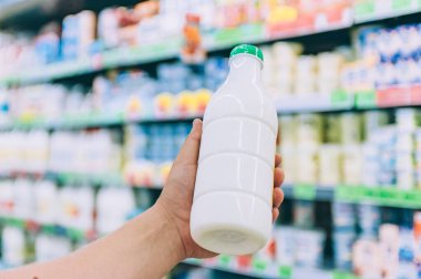 Bir adam süpermarkette elinde plastik bir şişede süt tutuyor.