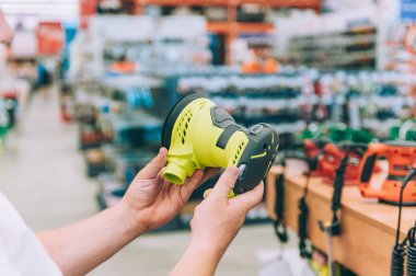 Adamın biri elinde zımpara makinesi tutuyor. Konsept adam bir hırdavatçıdan ürün seçer.