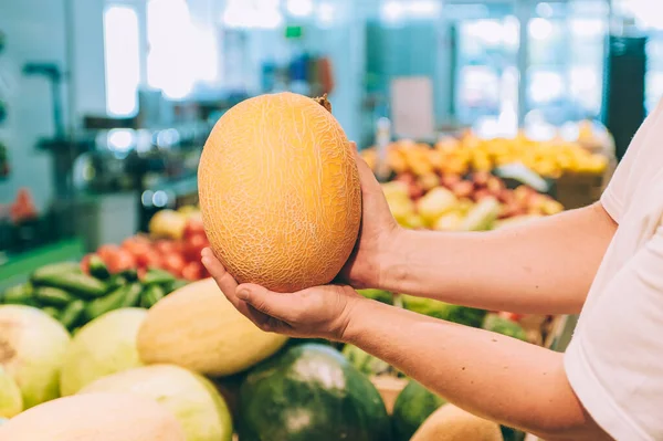 Süpermarkette elinde kavun tutan bir adam.