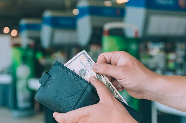 A man holds a wallet with dollars in his hand against the background of cash registers in the supermarket