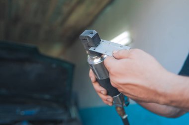 Adam elinde pnömatik bir alet tutuyordu. Garajda araba bakımı ve onarımı.