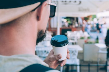 Adam bir kafede plastik bardakta kahve içiyor.