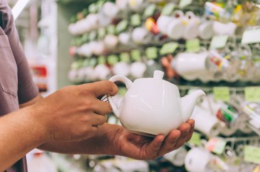 Süpermarkette bir adam elinde seramik bir çaydanlık tutuyor.