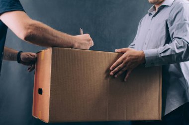 Karton kutulu bir adam bir müşteriye bir paket verir. Koyu arkaplanda teslimat hizmeti kavramı