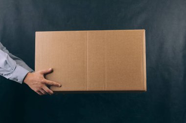 Elinde karton kutu olan bir adam. Koyu arkaplanda teslimat hizmeti kavramı