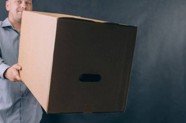Elinde karton kutu olan bir adam. Koyu arkaplanda teslimat hizmeti kavramı