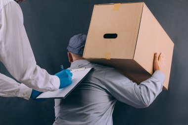 Elinde karton kutu ve elinde belgeler olan bir adam paketi müşteriye teslim ediyor. Koyu arkaplanda teslimat hizmeti kavramı