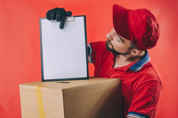 Elinde karton kutu olan bir adam. Kırmızı arkaplanda teslimat hizmeti kavramı