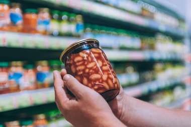 Süpermarketteki adam elinde cam bir kavanoz fasulye tutuyor.