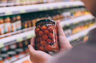 Süpermarketteki adam elinde domatesli cam bir kavanoz tutuyor.
