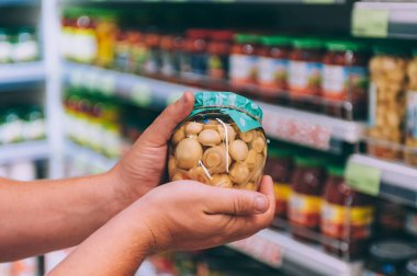Süpermarketteki adam elinde mantarlı cam bir kavanoz tutuyor.