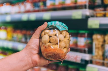 Süpermarketteki adam elinde mantarlı cam bir kavanoz tutuyor.