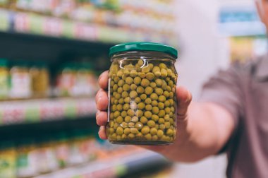 Süpermarketteki adam elinde bezelyeli cam bir kavanoz tutuyor.