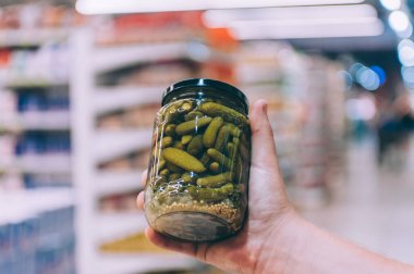 Süpermarketteki adam cam bir salatalık kavanozu tutuyor.